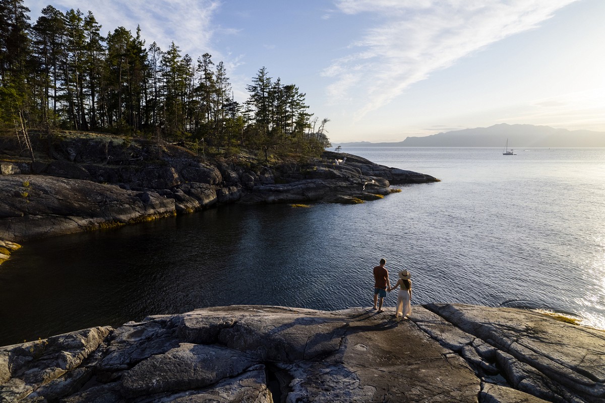 A man and a woman hold hands while standing near the shoreline on Vancouver Island