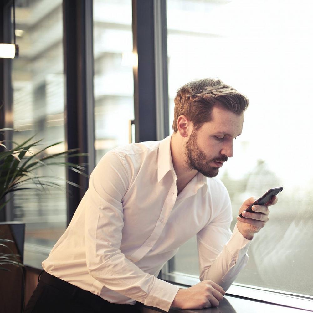 A man wearing business attire looking at his phone, considering calling Recovery Coach Michael Walsh to discuss stopping or cutting down on drug or alcohol use